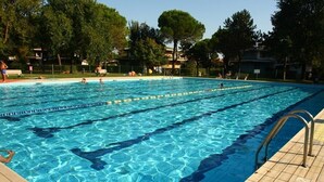 Una piscina con acqua cristallina blu, circondata da alberi e un solarium piastrellato.