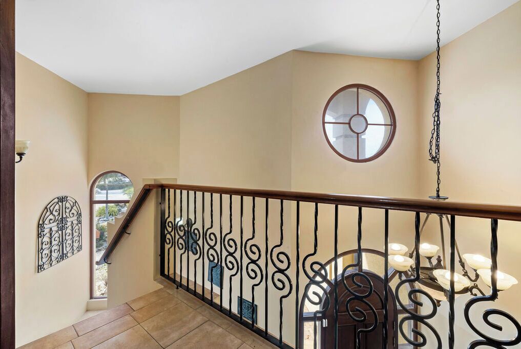 A staircase with ornate black railings, a round window with a white frame, and a chandelier.