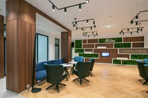 Un hall d’hôtel moderne comprenant un comptoir d’accueil, un espace salon et un mur agrémenté de plantes et de panneaux d’affichage.