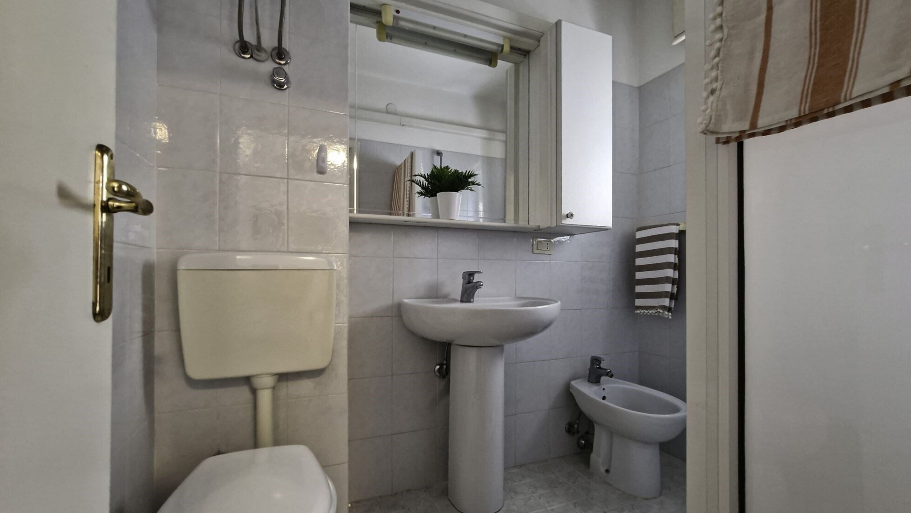 Un baño con inodoro, lavamanos, bidé y espejo sobre el lavamanos.