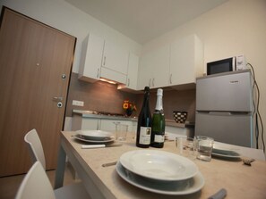 A compact kitchen with white cabinets, a microwave, and a refrigerator. There are two bottles of wine and a bowl on the counter. - Welcoming Apartment-beahost Rentals (Rosolina)