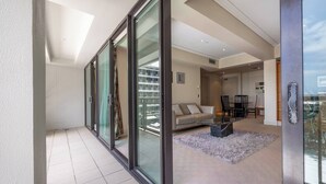 Un salon moderne avec un canapé, une table basse et une vue sur un balcon, accessible par de grandes portes vitrées.