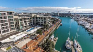 Un port de plaisance avec des bateaux amarrés, un bâtiment moderne à plusieurs étages et un ciel dégagé.