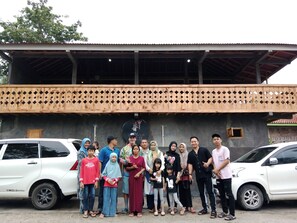 A group of people standing in front of a building with a wooden lattice balcony and a sign with Chinese characters.