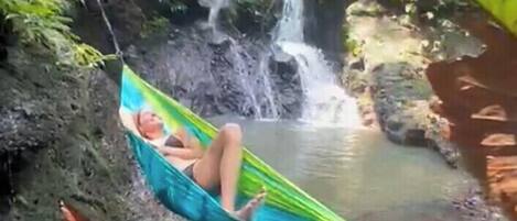 A hammock in a natural setting with a waterfall and greenery.