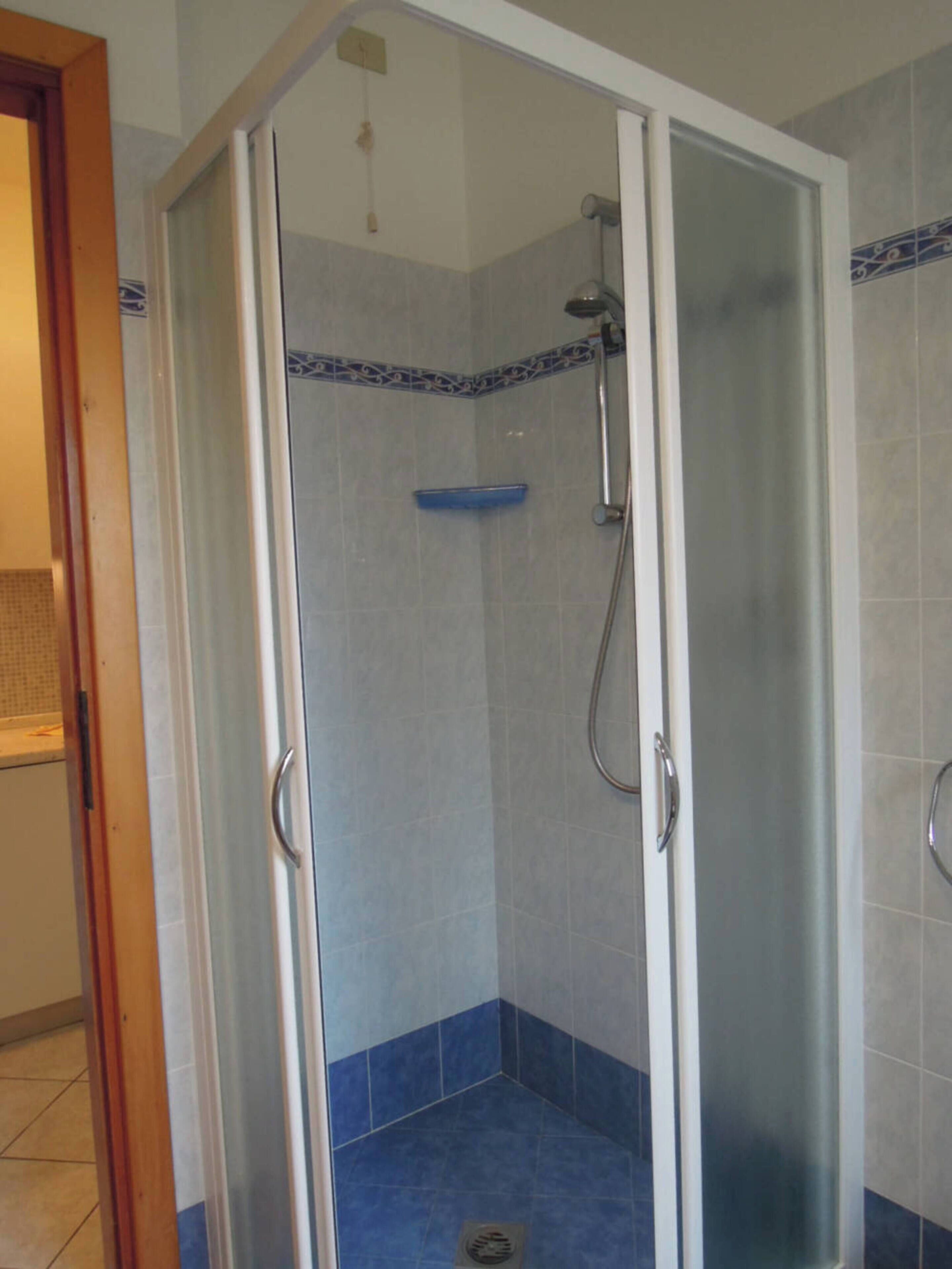 Eine bodenebene Dusche mit Glastür, blauen Fliesen und Duschkopf.