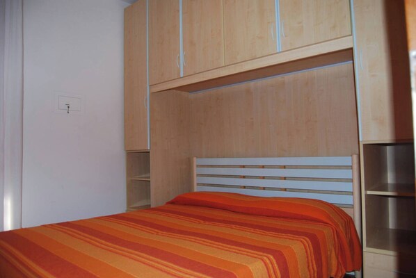 A single bed with a striped bedspread, wooden headboard, and built-in wooden shelving above.