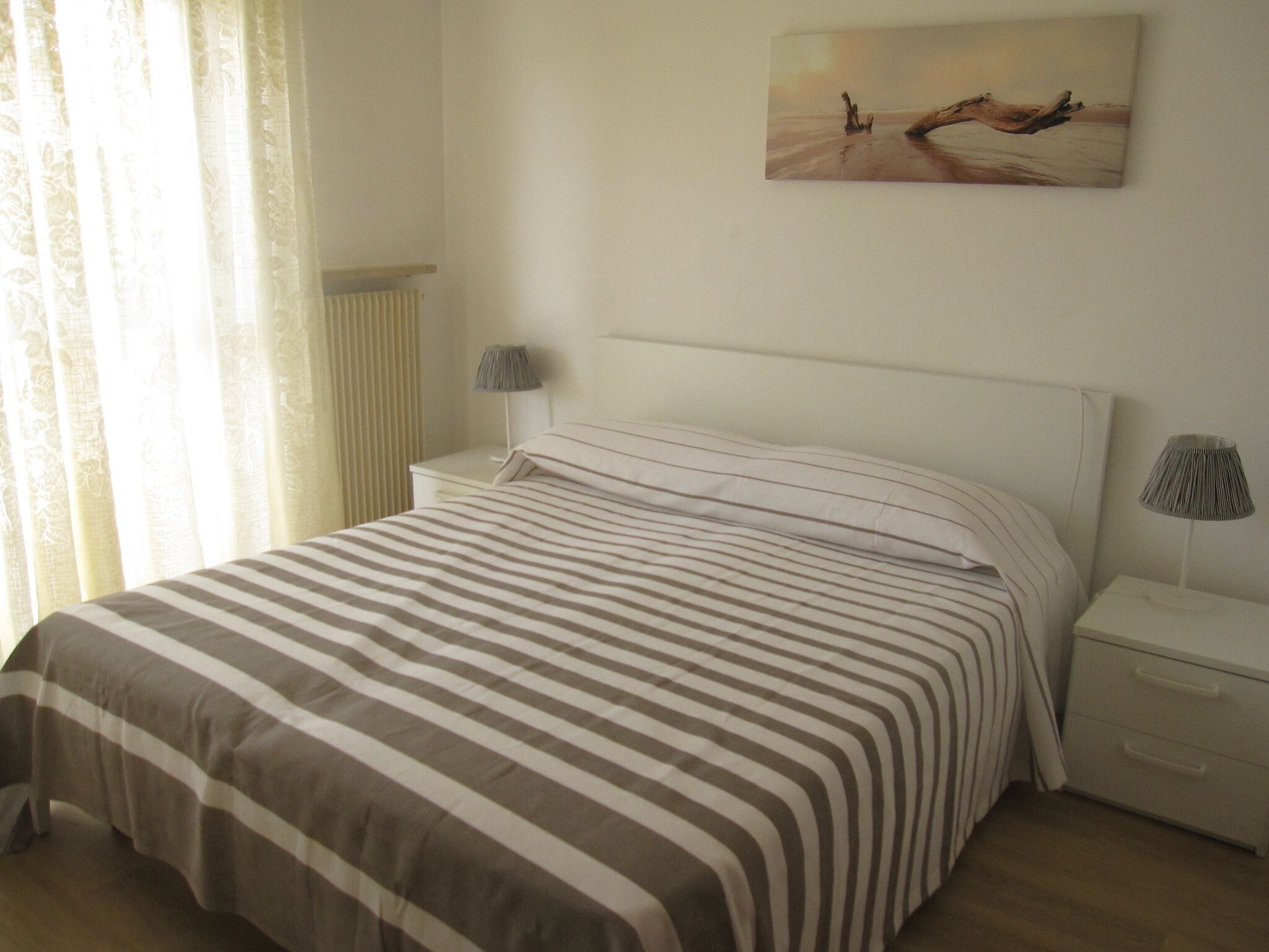 A neatly made bed with striped bedding, a bedside lamp, and a painting on the wall.
