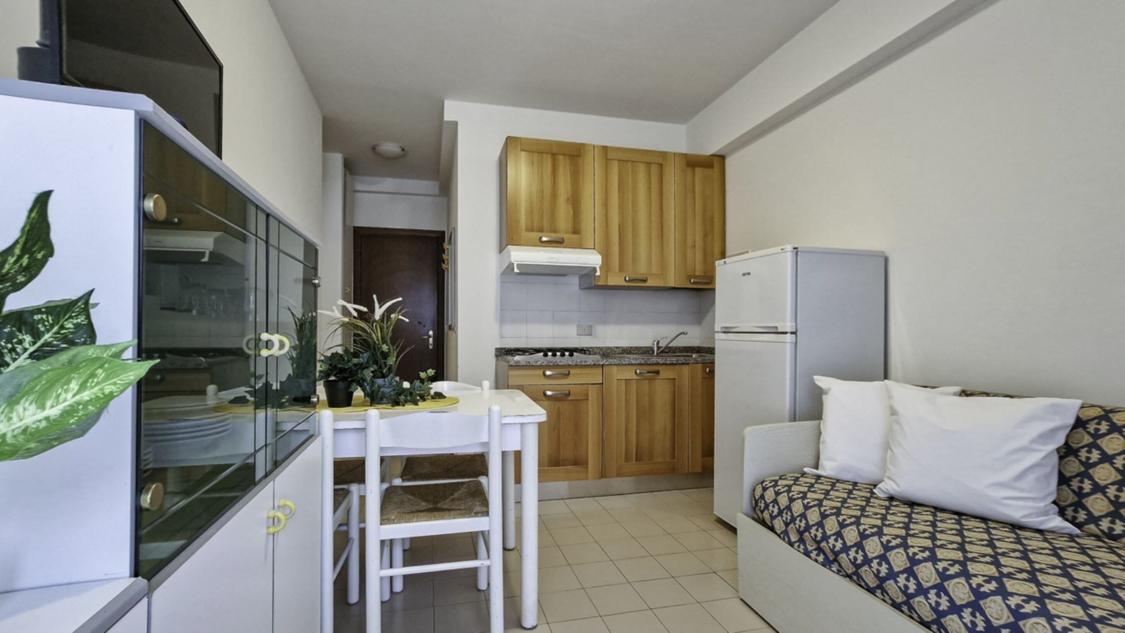 A compact kitchen with wooden cabinets, a white refrigerator, and a dining area with a table and chairs.