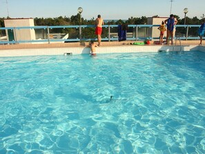 A swimming pool with clear blue water, a tiled deck, and a railing.