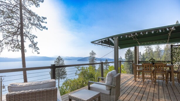 Eine Holzterrasse mit Korbmöbeln, mit Blick auf einen See und Berge.