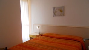 A single bed with an orange blanket, a bedside table with a lamp, and a wall-mounted artwork.