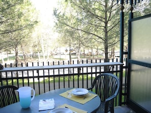 A table with a pitcher, plates, and a glass on a balcony with a view of trees and a fence. - Flat in Residence With Swimming Pool and Balcony (San Michele al Tagliamento)