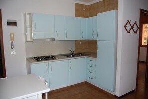 Uma cozinha compacta com armários azul-claros, bancada branca e fogão a gás.