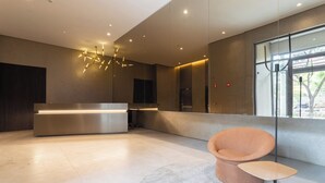 A modern reception area with a reception desk, a round seating area, and a large window providing natural light. - House of Charlie Paraíso (São Paulo)