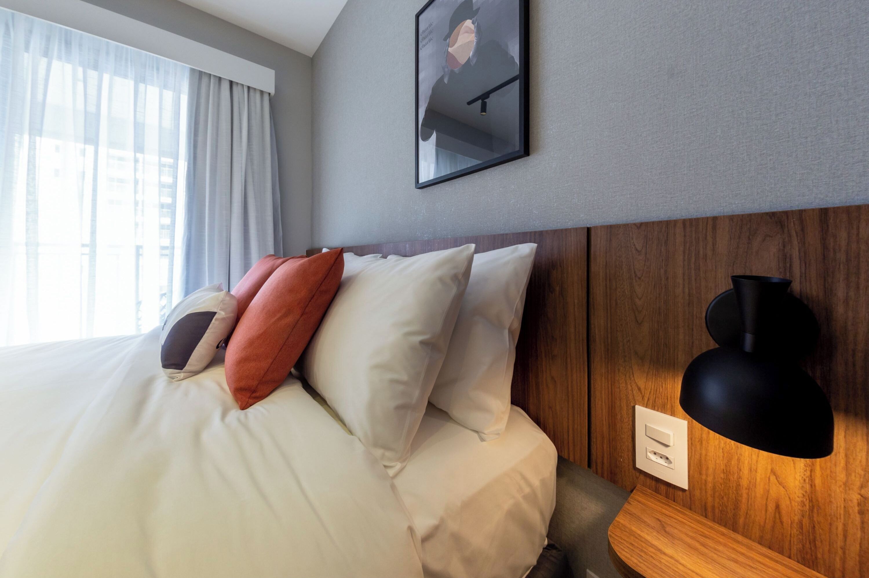 A hotel room with a bed, a wall-mounted lamp, and a framed picture.