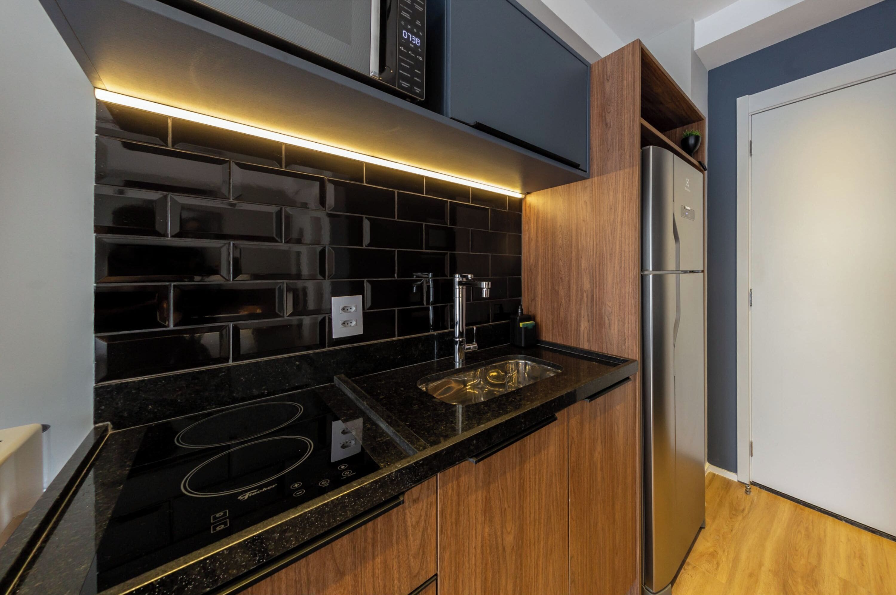 Una cocina moderna con encimeras negras, armarios de madera, un refrigerador de acero inoxidable y un microondas integrado.