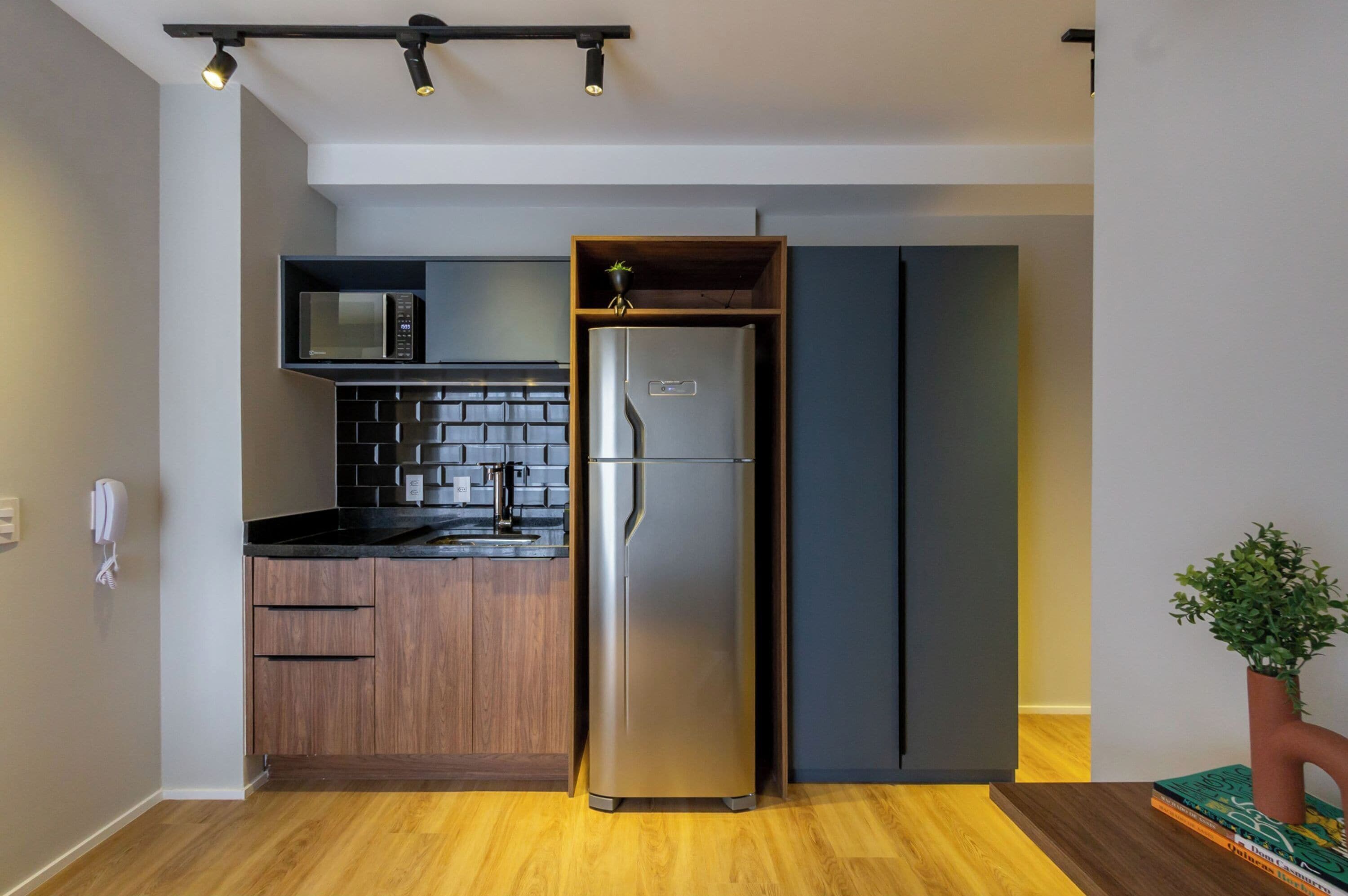 Una cocina moderna con microondas integrado, refrigerador de acero inoxidable, armarios de madera y encimera negra.