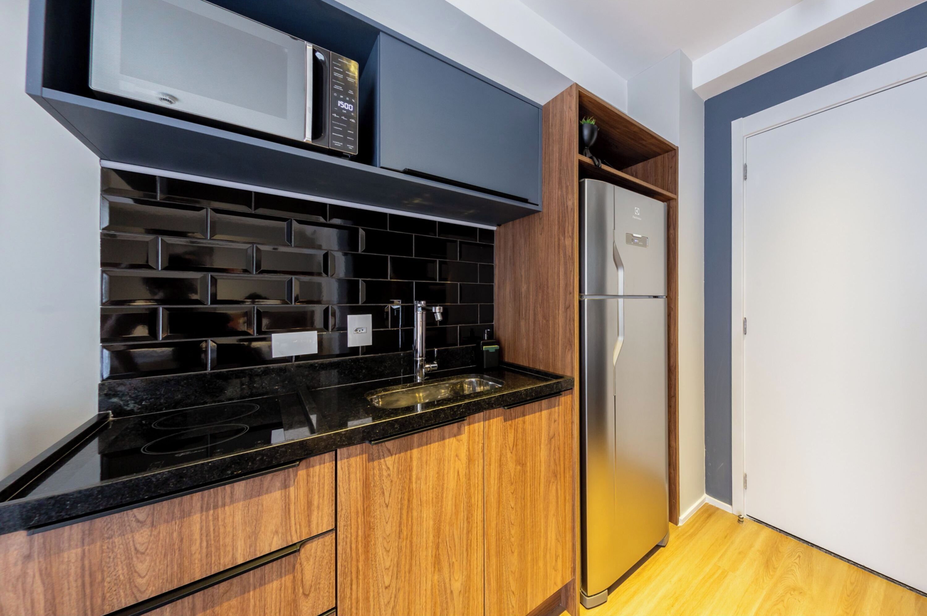 Una cocina moderna con encimeras negras, armarios de madera, un refrigerador de acero inoxidable y un microondas.