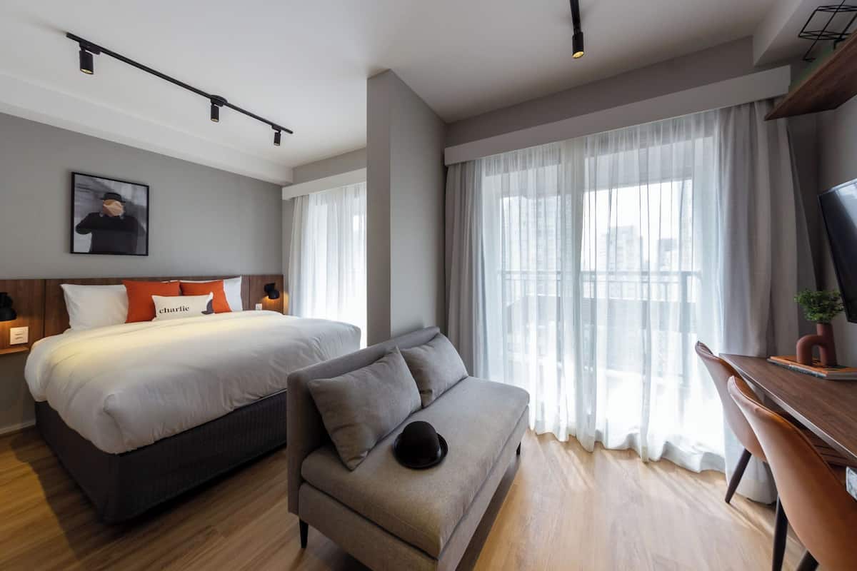 Ein modernes Hotelzimmer mit einem großen Bett, einer Sitzecke, einem Fernseher und einem Fenster mit durchsichtigen Vorhängen.