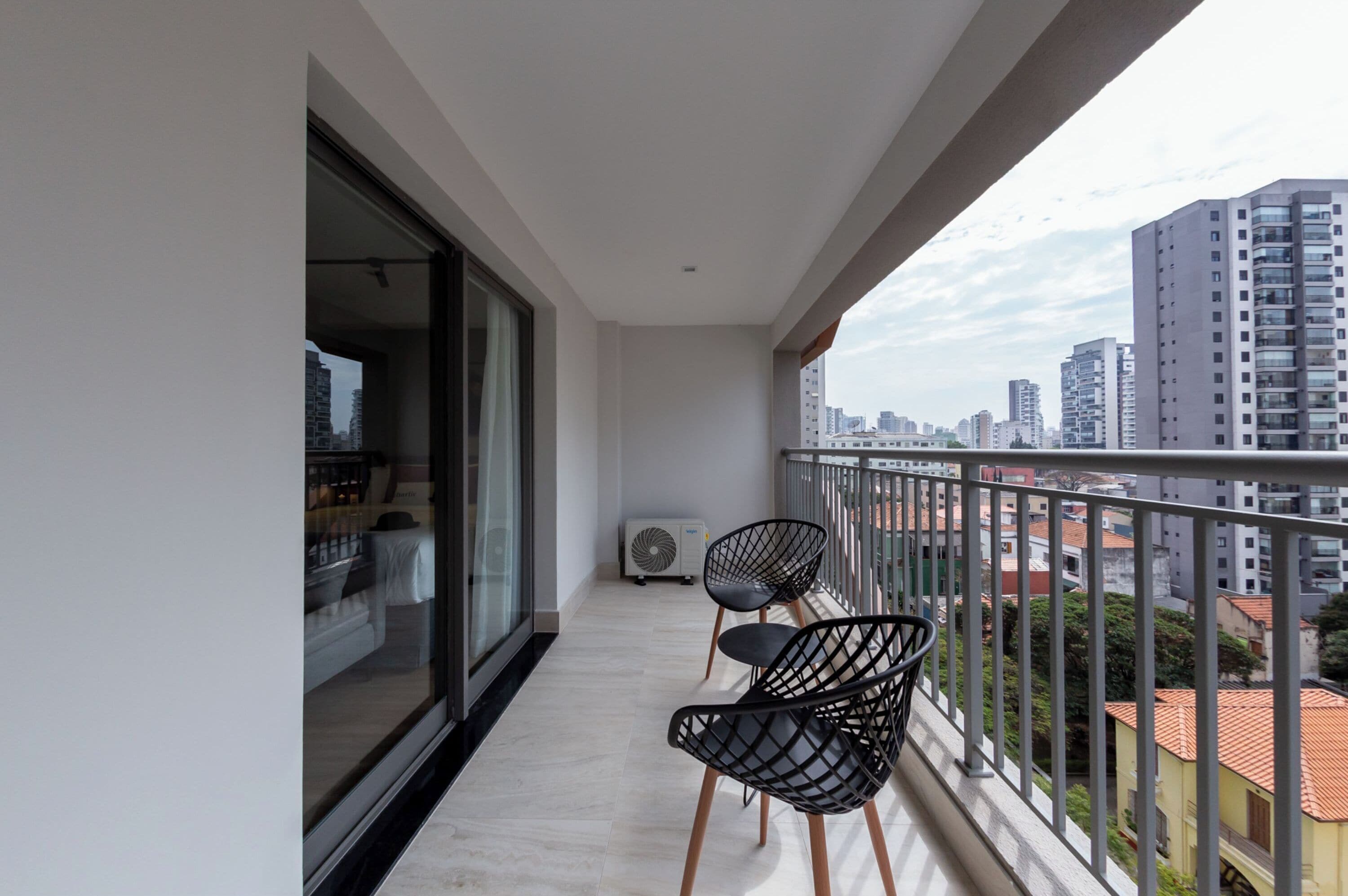 A balcony with two black chairs, a glass door leading to a room, and a view of city buildings.