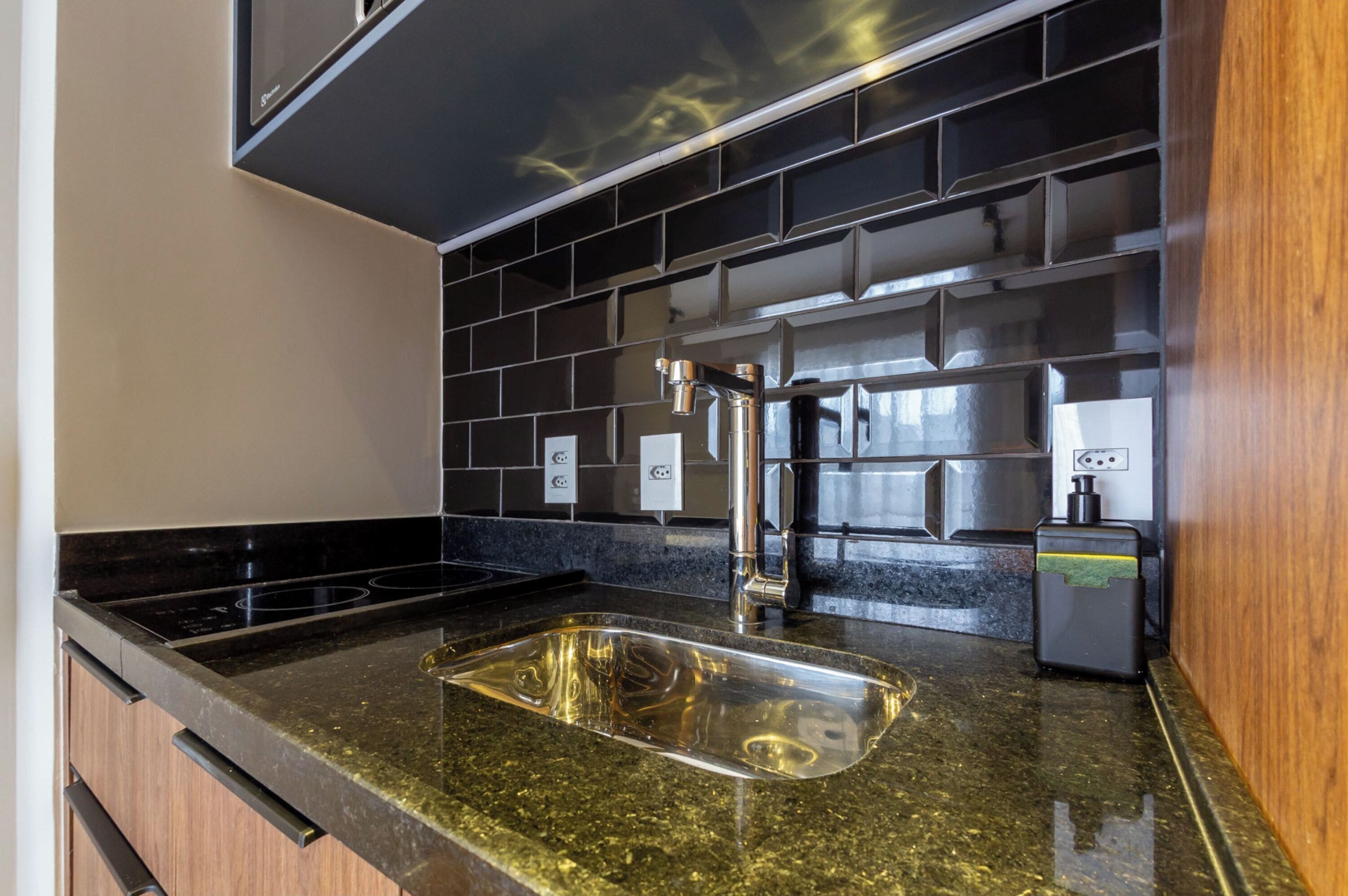 A kitchen with a black tiled backsplash, stainless steel sink, and a built-in stove.