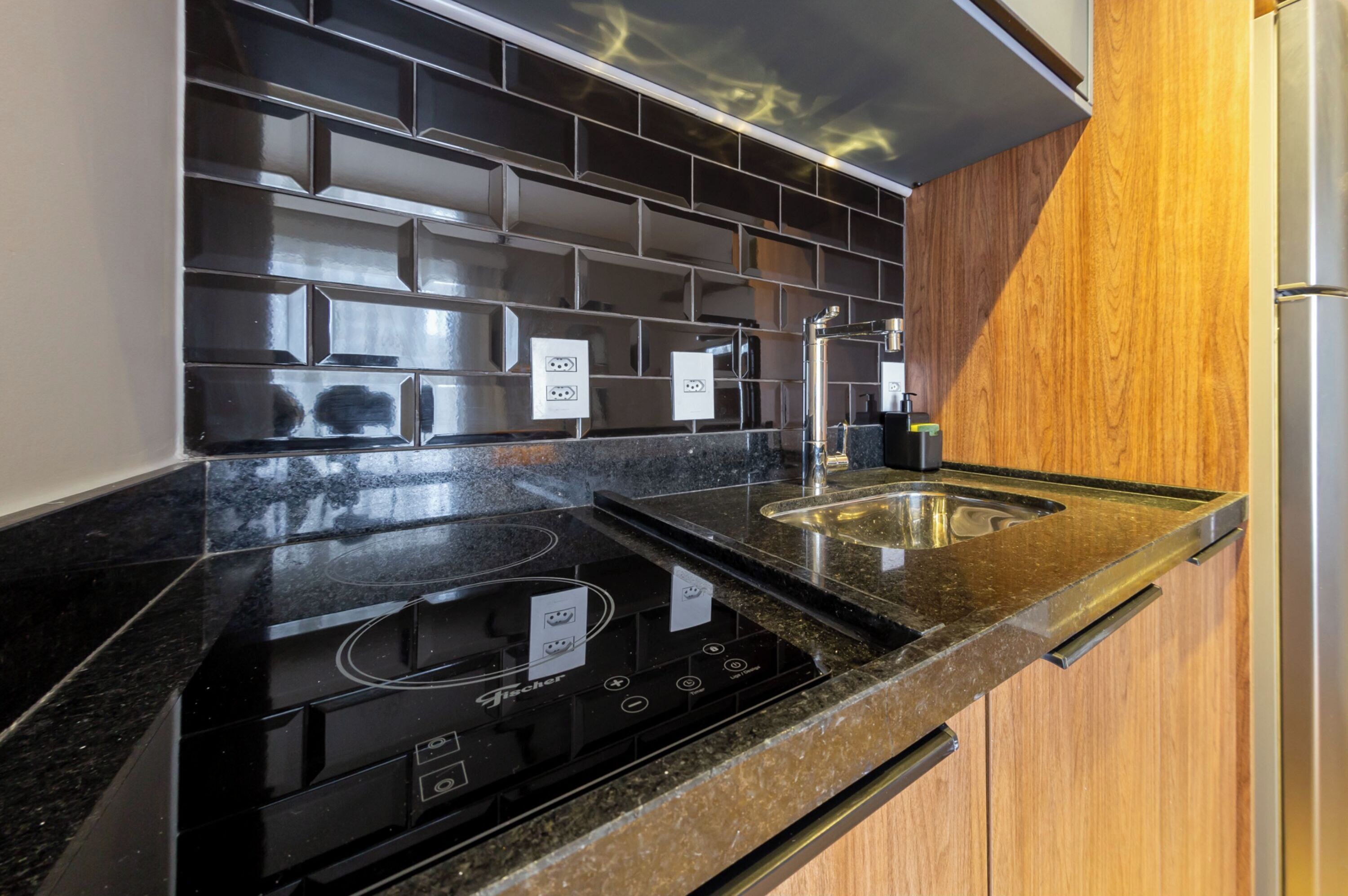 Una cocina con salpicadero de azulejos negros, electrodomésticos de acero inoxidable y armarios de madera.
