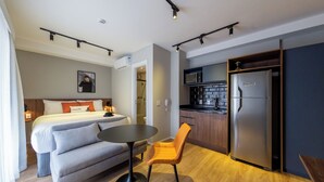 A modern hotel room with a bed, a sofa, a dining table, a chair, a kitchen area with a refrigerator, and a microwave. - House of Charlie Paraíso (São Paulo)