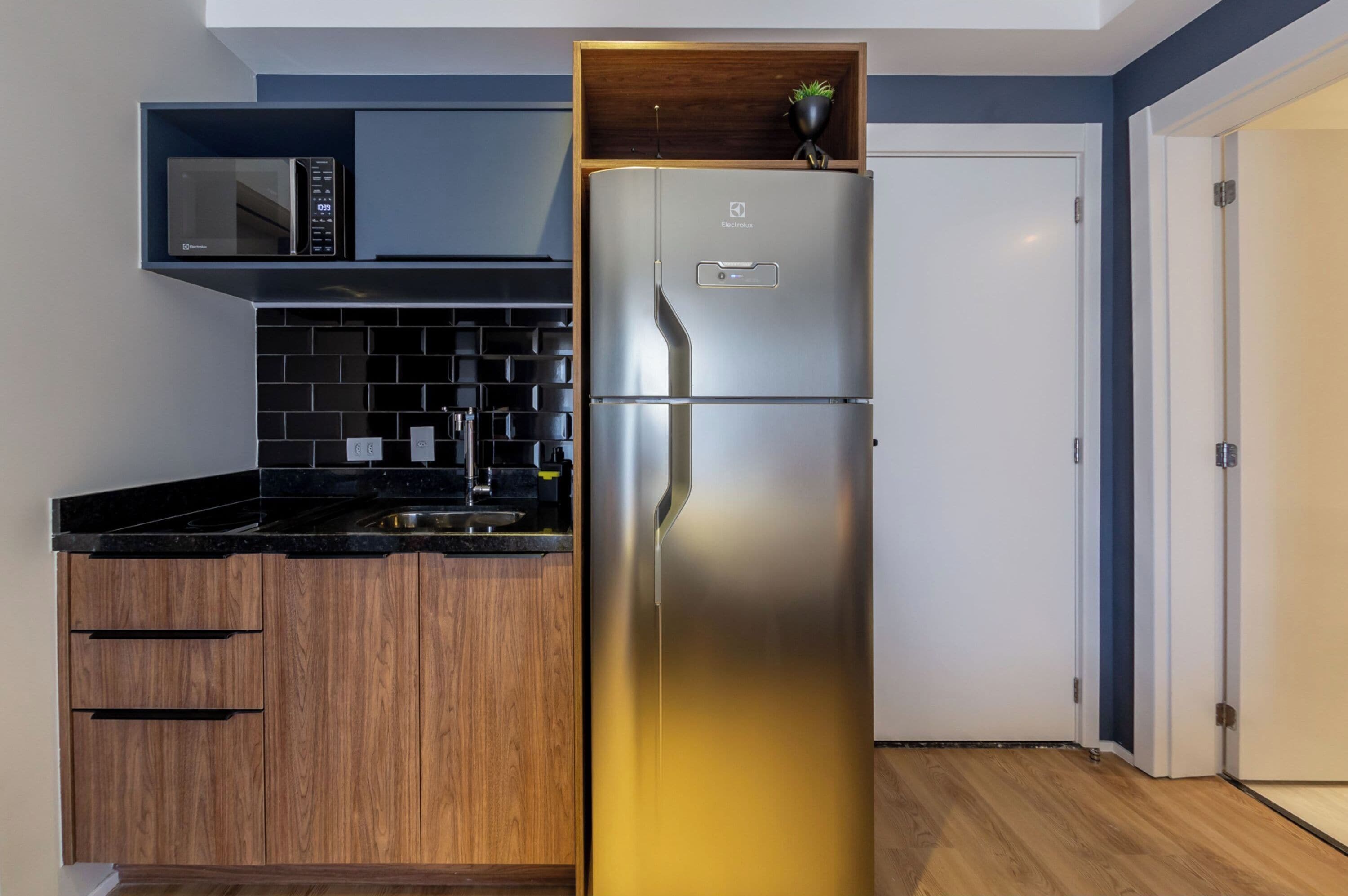 Eine Küche mit einem Edelstahl-Kühlschrank, einer Mikrowelle, Holzschränken und einer schwarzen Arbeitsplatte.