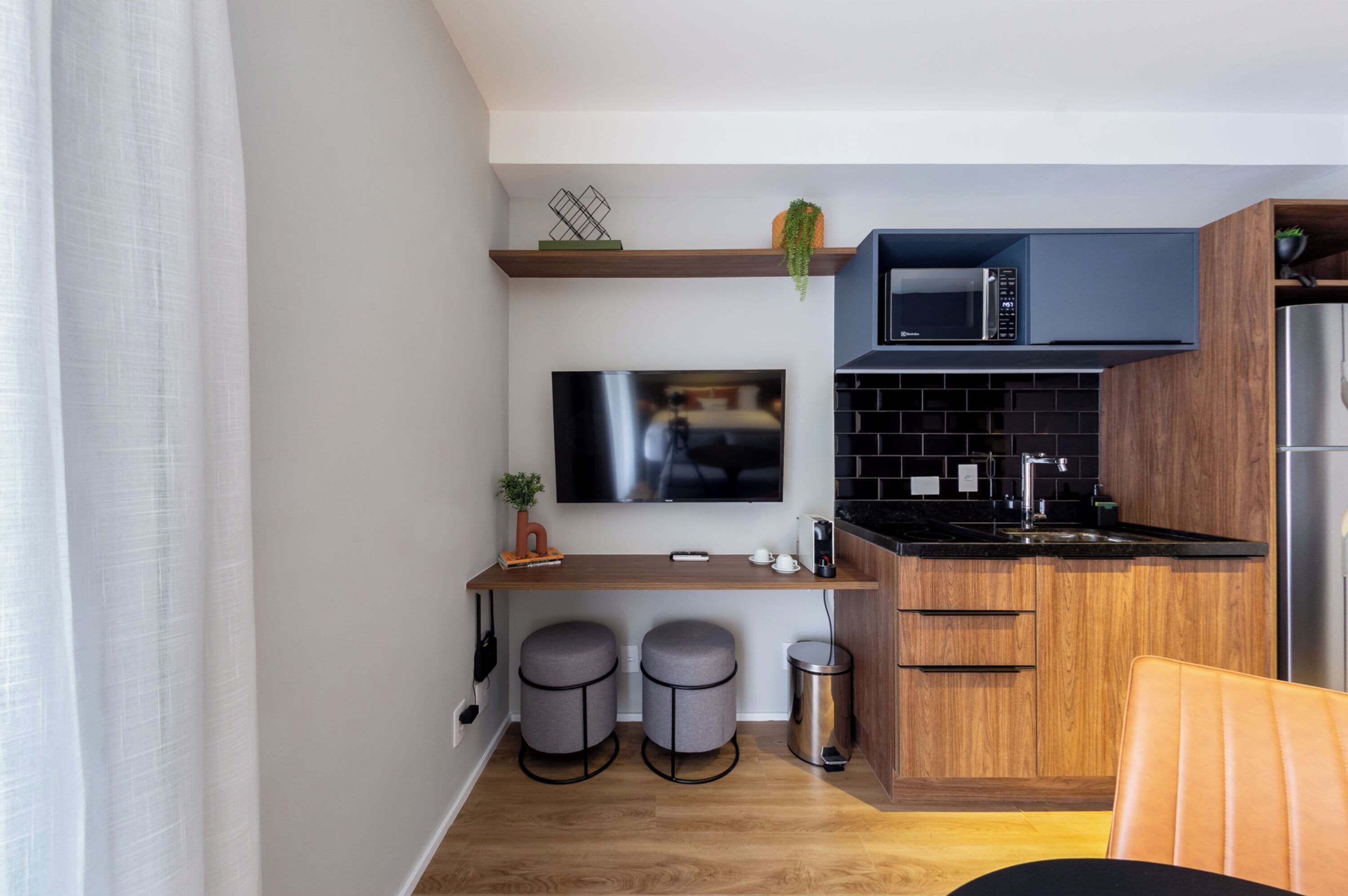Een moderne keuken met een flatscreen televisie, houten kastjes, een magnetron en een roestvrijstalen koelkast.