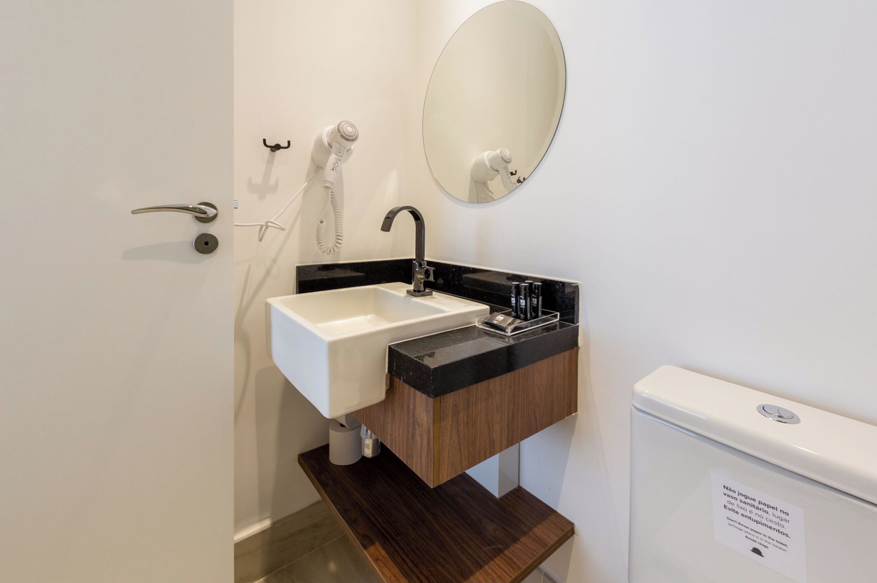 Un baño moderno con un lavamanos blanco, encimera negra y tocador de madera.