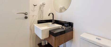 Un baño moderno con un lavamanos blanco, encimera negra y tocador de madera.