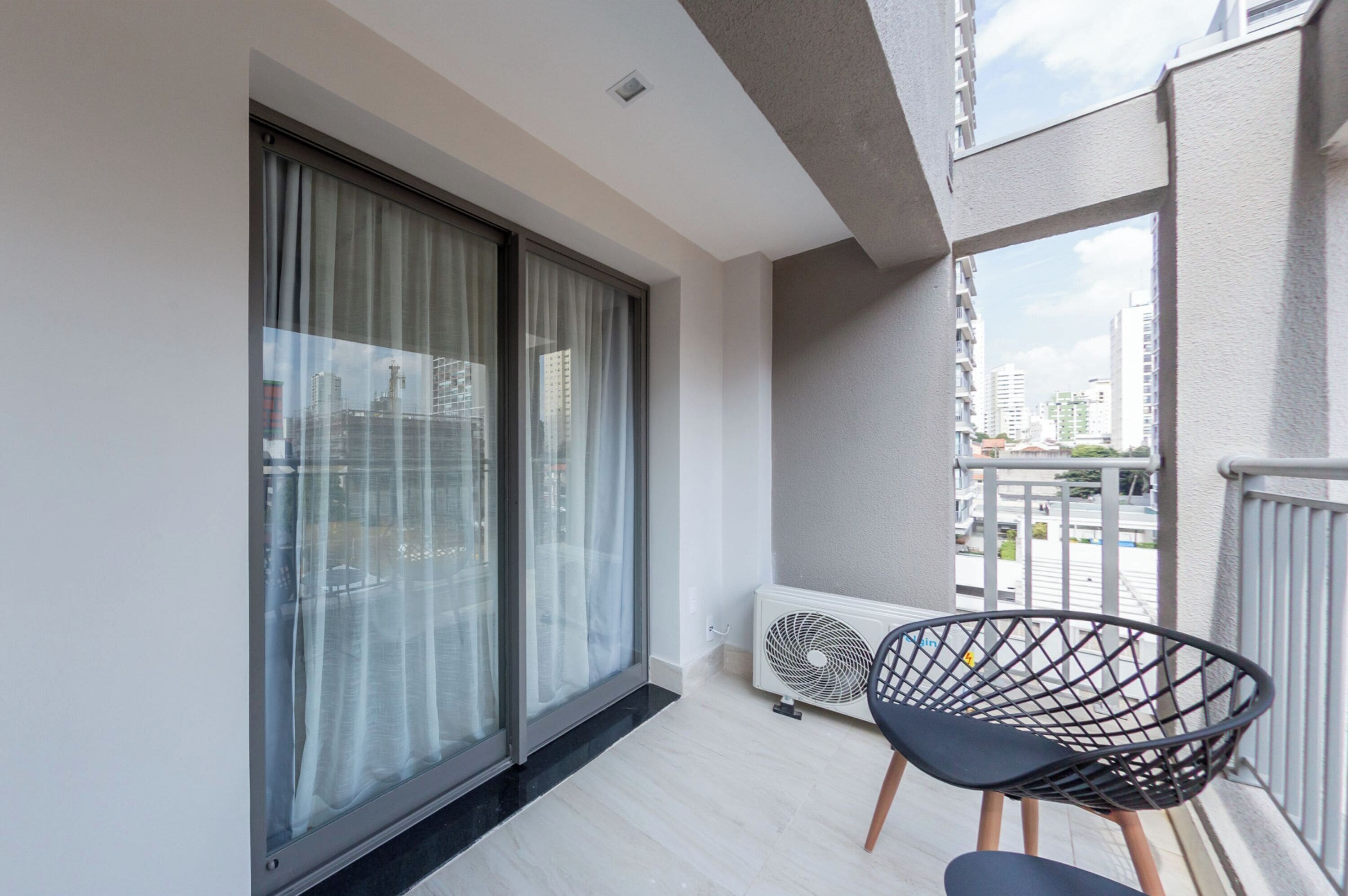 A balcony with a sliding glass door, a standing fan, and a black wireframe chair.