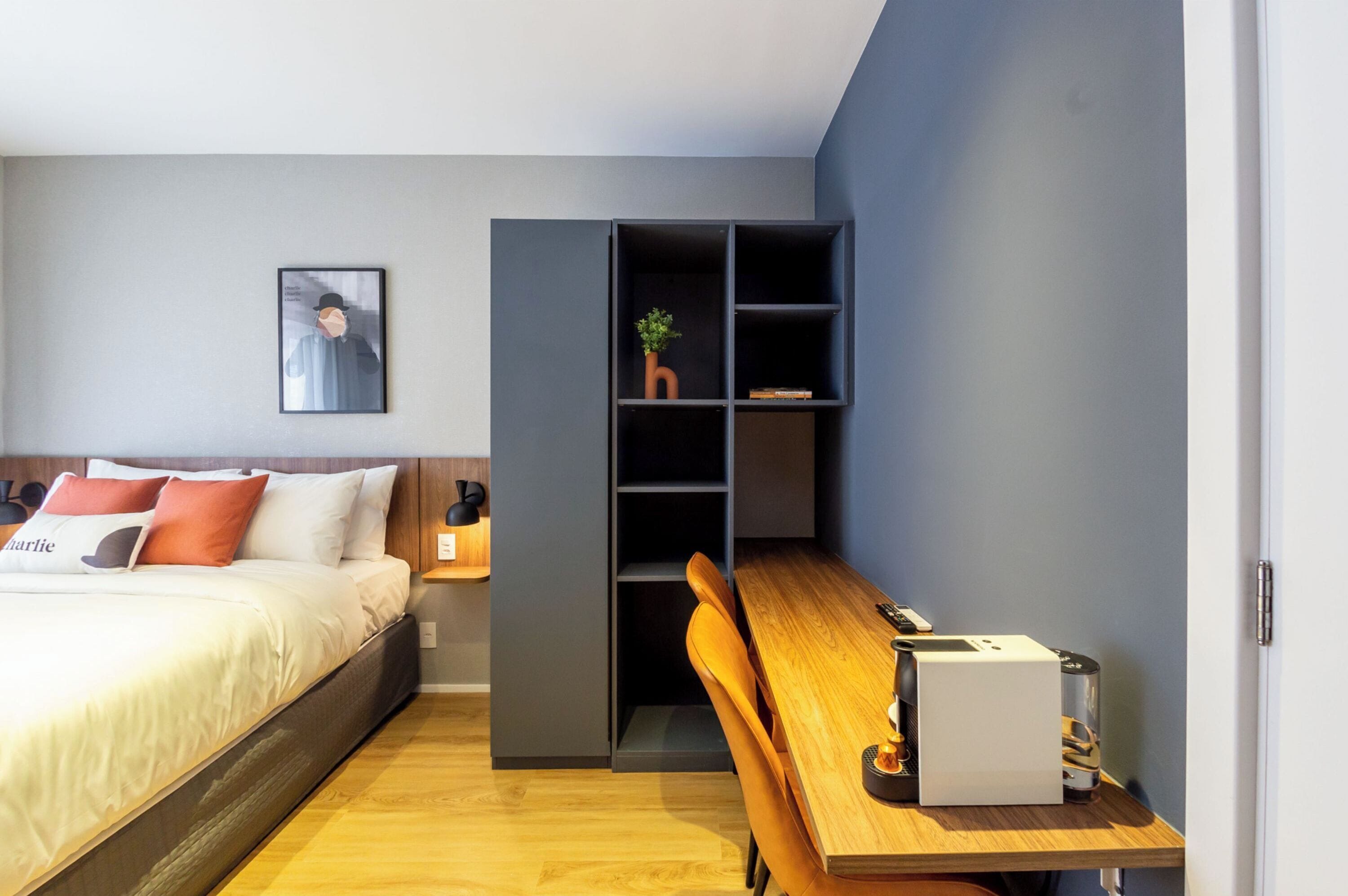 A modern bedroom with a bed, a desk, and a shelving unit.