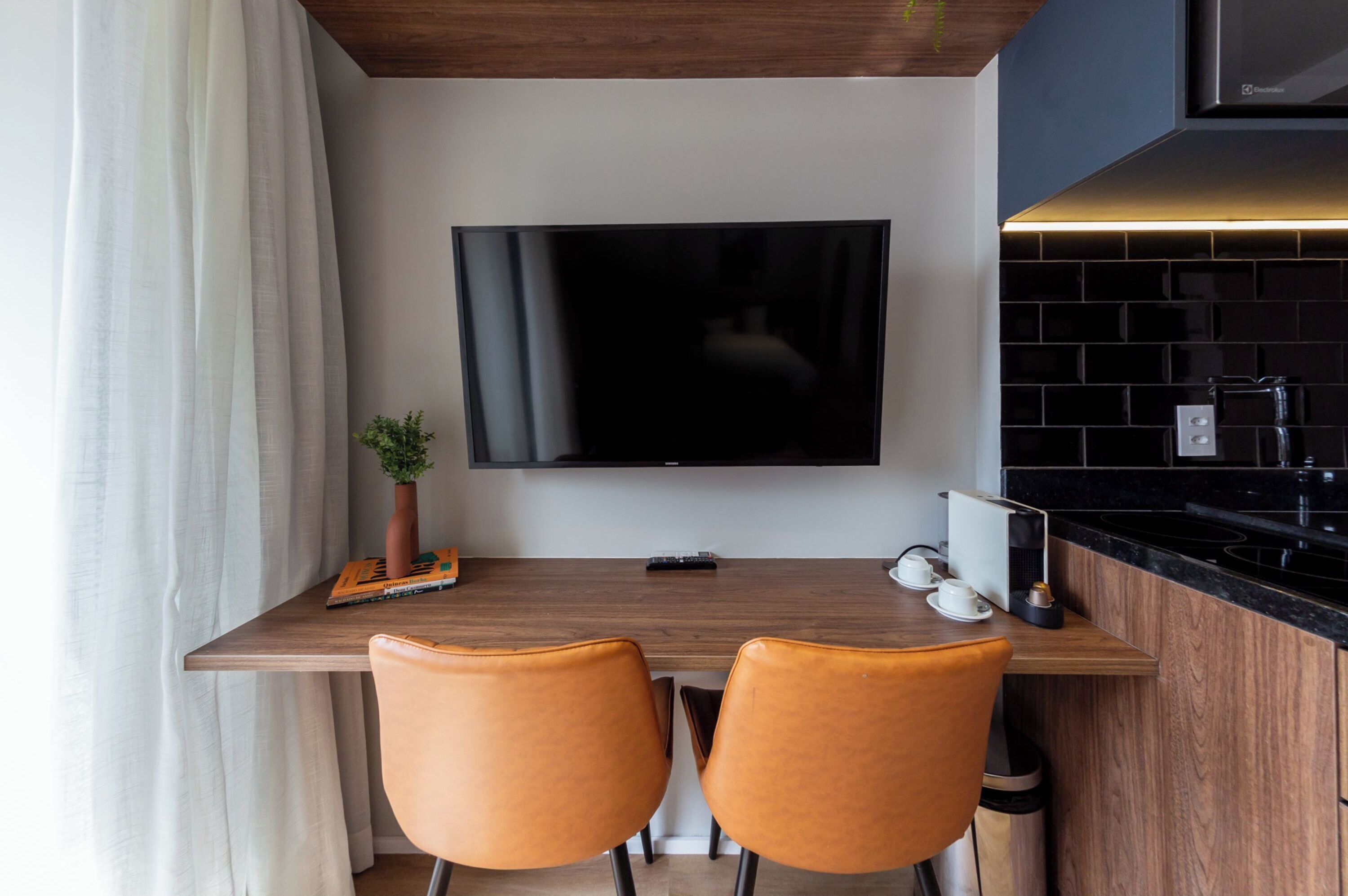 A modern kitchen with a flat-screen TV mounted above a wooden dining table with two chairs.