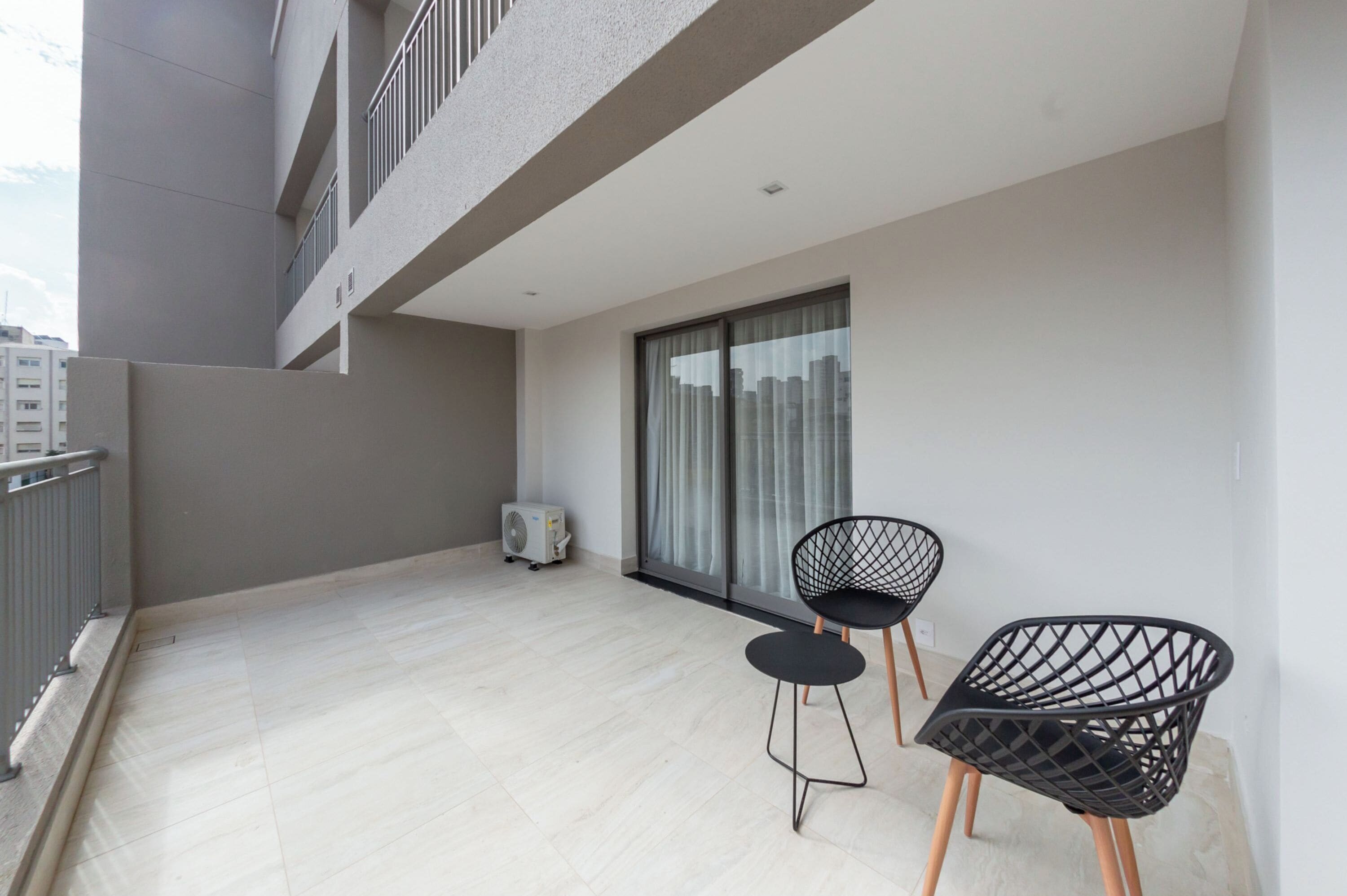 A balcony with two black chairs, a sliding glass door, and a white air conditioning unit.