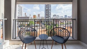 A balcony with two black chairs and a small table, overlooking a cityscape with various buildings and construction sites. - House of Charlie Paraíso (São Paulo)
