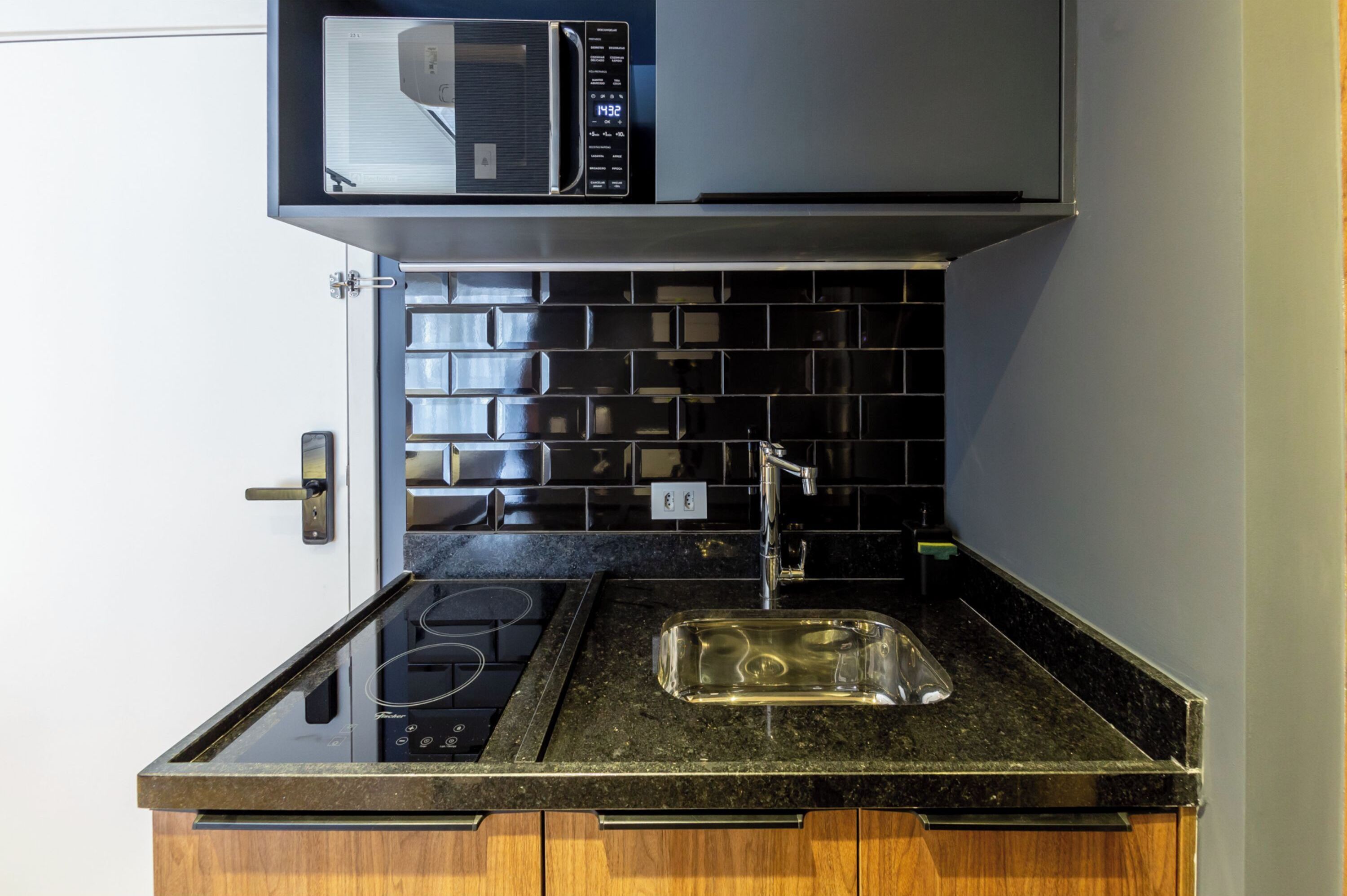 Une cuisine compacte équipée d’un four à micro-ondes encastré, d’une cuisinière à gaz, d’un évier et d’un dosseret de carrelage noir.