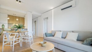 Ein modernes Wohnzimmer mit einer grauen Couch, weißen Sesseln und einem runden Holztisch.