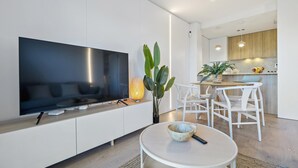 Ein modernes Wohnzimmer mit einem Flachbildfernseher, einem runden Couchtisch und weißen Möbeln.