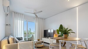 Ein modernes Wohnzimmer mit einer Couch, einem Esstisch mit Stühlen, einem Fernseher und einem Deckenventilator.