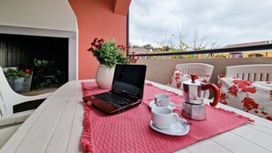 A balcony with a laptop, two cups, a coffee pot, and a potted plant. - Modern Apartment With Swimming Pool (San Michele al Tagliamento)