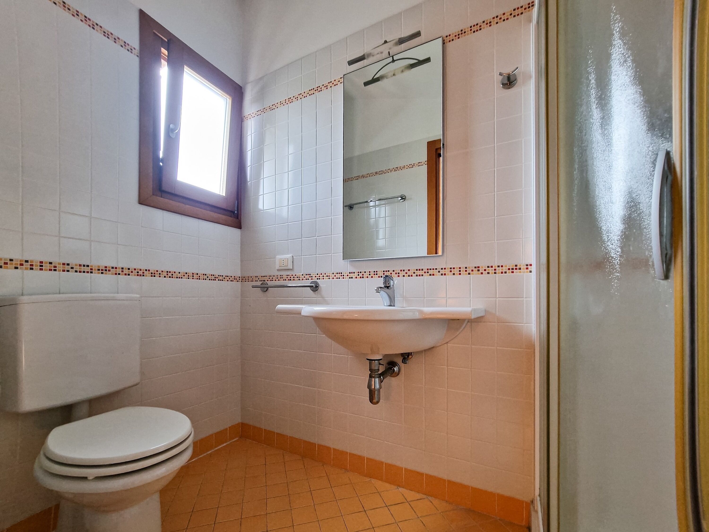 A bathroom with a toilet, sink, mirror, and a window.