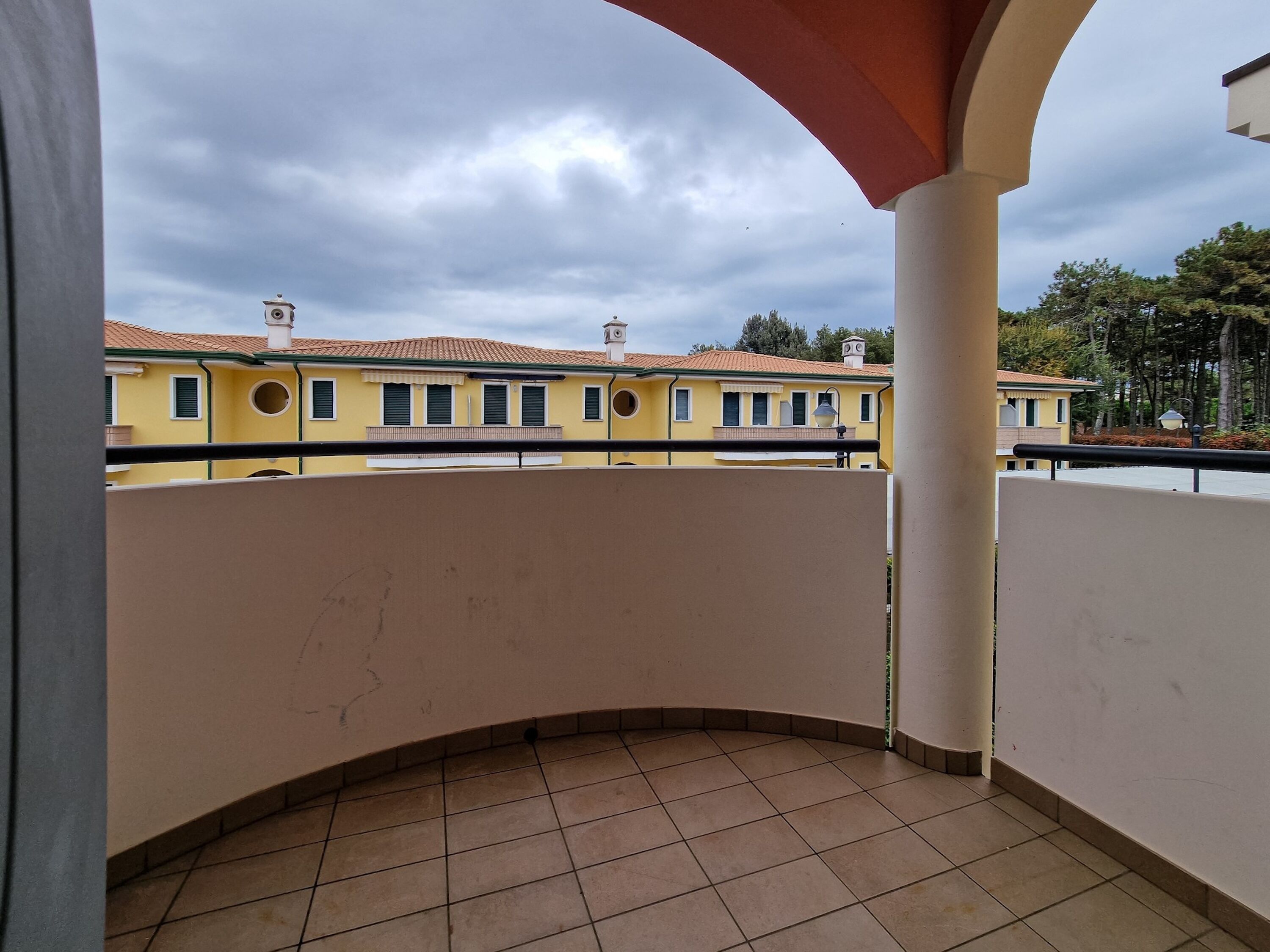 Ein Balkon mit Fliesenboden, einer gewölbten Geländer und Blick auf gelbe Gebäude mit Fenstern und Schornsteinen.