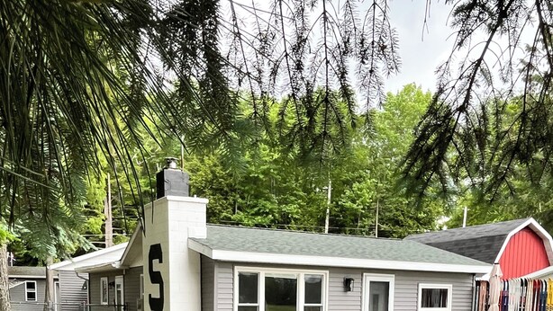Une petite maison avec un patio couvert, un barbecue et, au fond, une grange rouge.