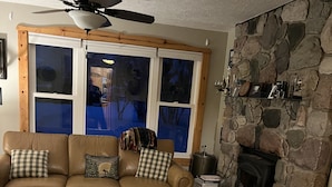 Un salon chaleureux avec une cheminée en pierre, une grande fenêtre et un ventilateur de plafond.