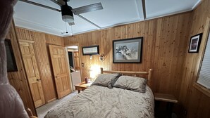 Une chambre avec des lambris en bois, un lit avec une literie à motifs, un ventilateur de plafond et un tableau encadré au mur.