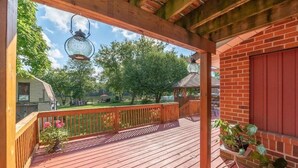 Une terrasse en bois avec une balustrade, un mur en briques et une vue sur un parc arboré, avec un kiosque.