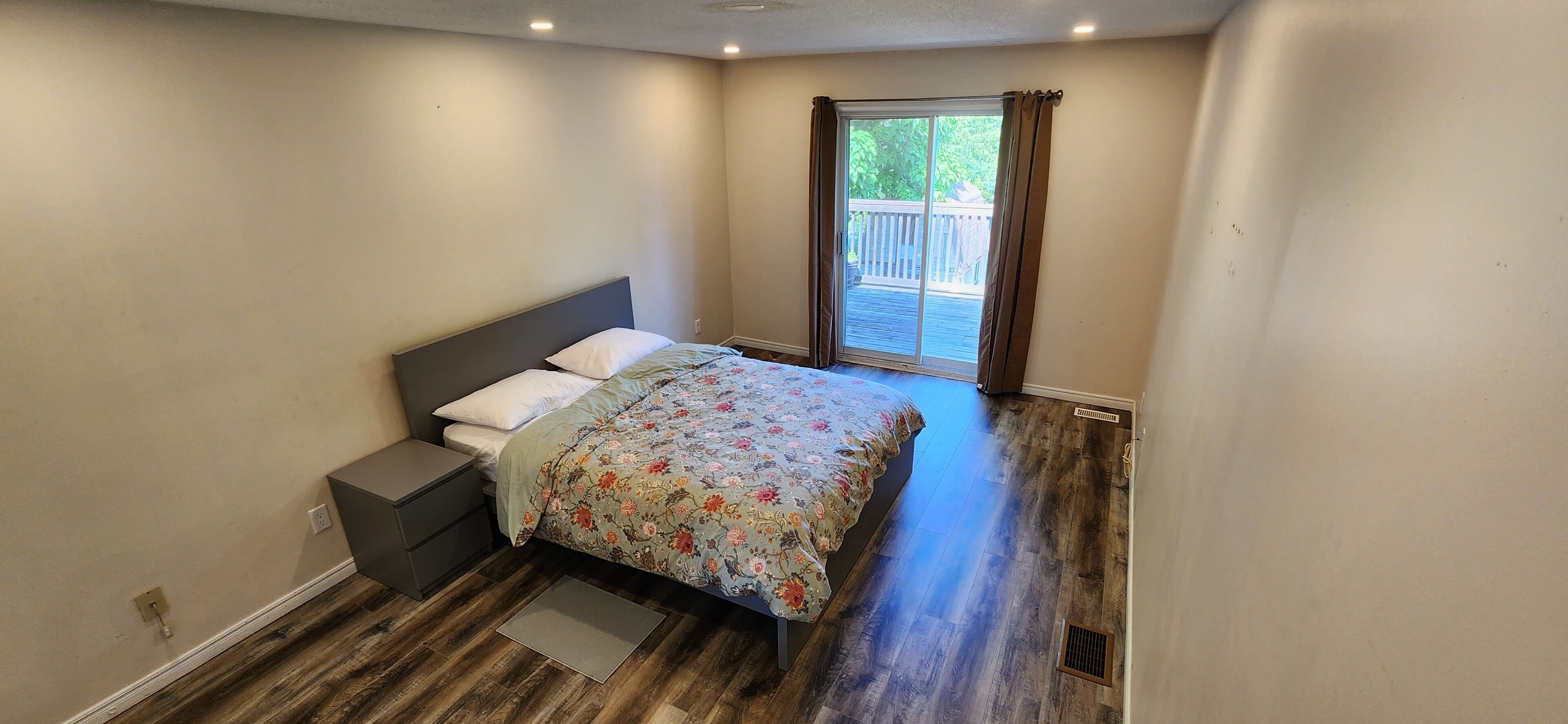 Een slaapkamer met een bed, nachtkastje en een raam met uitzicht op een terras.