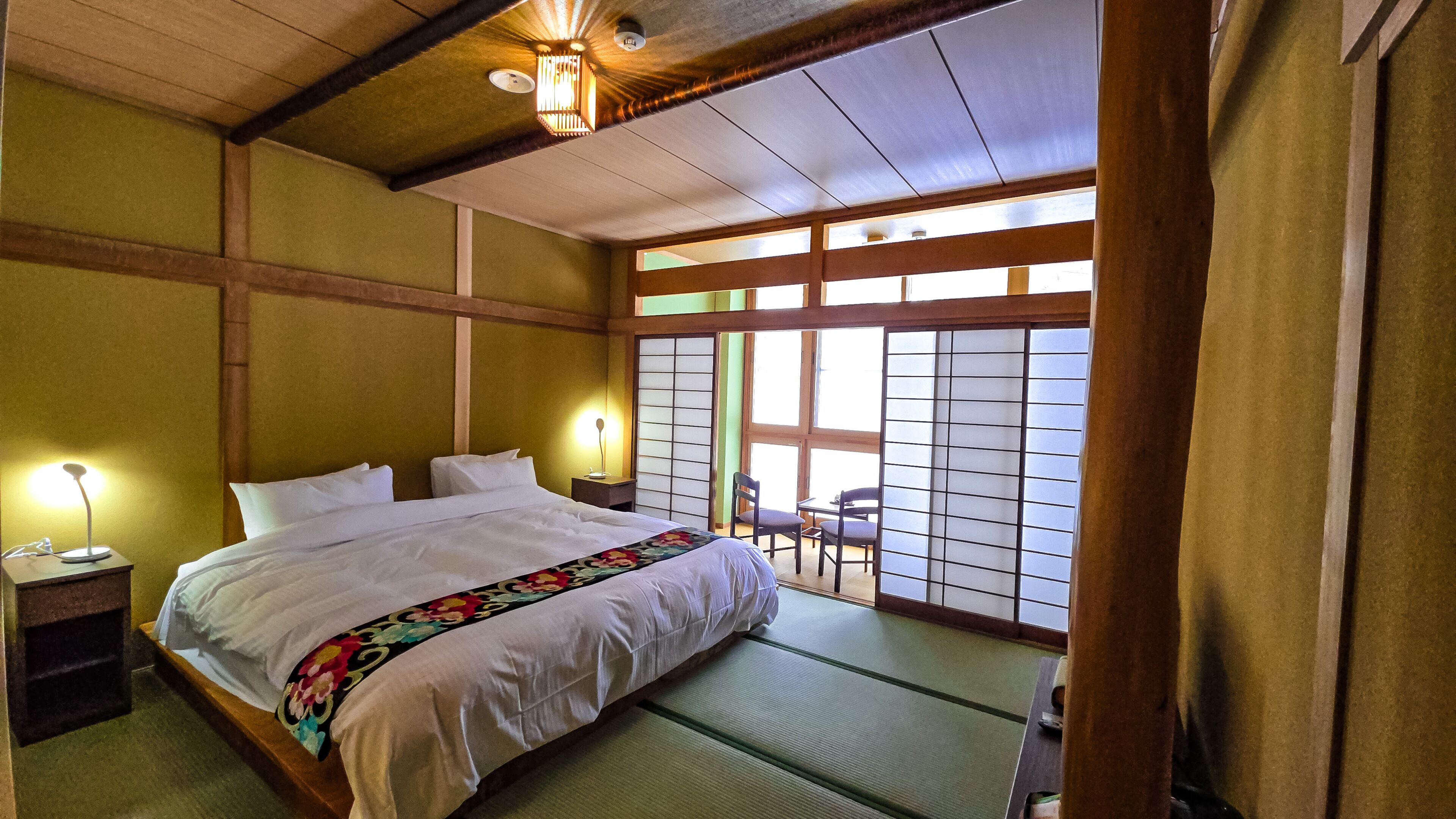 Een traditionele Japanse slaapkamer met tatami vloeren, een groot bed met witte beddengoed en verschuifbare shoji deuren.